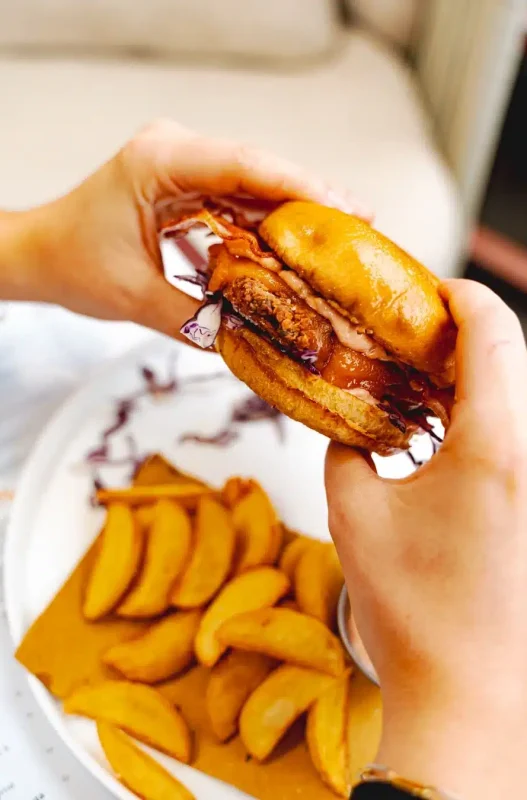 persona che ha in mano un hamburger con sotto delle patatine fritte